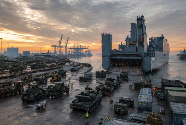 U.S. military vehicles and armored equipment loading onto a strategic sealift ship at a port during large-scale logistics operations